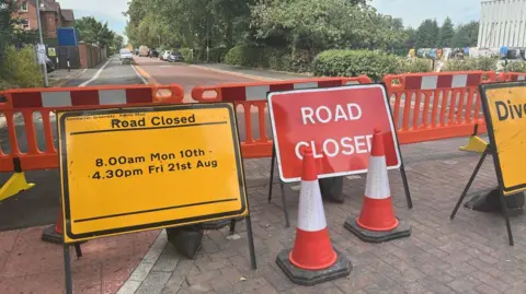 Road closure signs, barriers and traffic cones with a red cycle street behind it.