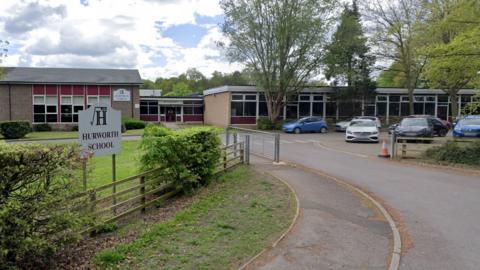 Exterior of Hurworth School, with signage and car park in front of a one-storey school block