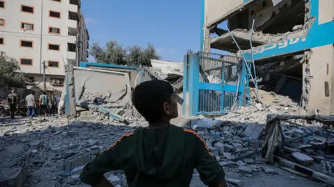 A Palestinian boy stands near the rubble of a damaged Unrwa-run school in Nuseirat refugee camp, central Gaza, following an Israeli air strike (14 July 2024)