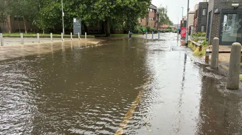 A town centre road submerged in water. The pavements on both sides of the road are dry.