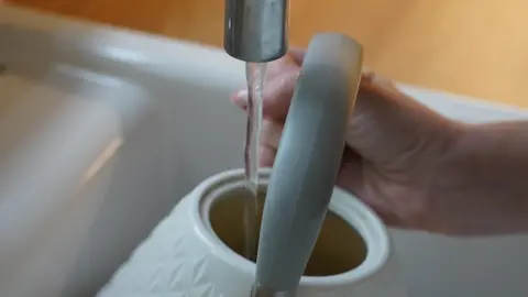A person filling up their kettle under the tap.