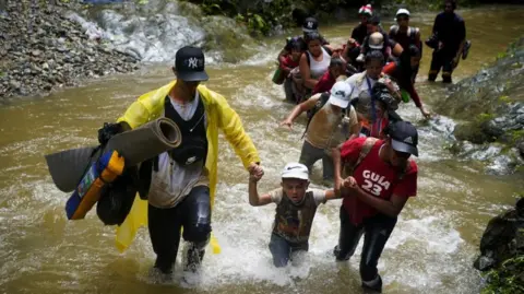 Reuters Sekelompok migran dari Venezuela, Ekuador dan Haiti menyeberangi sungai Rio Muerto di Darien Gap, saat mereka melanjutkan perjalanan menuju perbatasan AS, di Acandi, Kolombia 9 Juli 2023