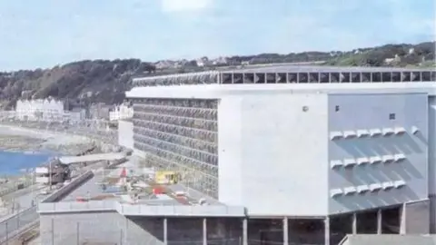 MANX NATIONAL HERITAGE A 70s image of the complex, a large white building with lots of glass windows, it is on the seafront, you can see the Douglas prom in the background.