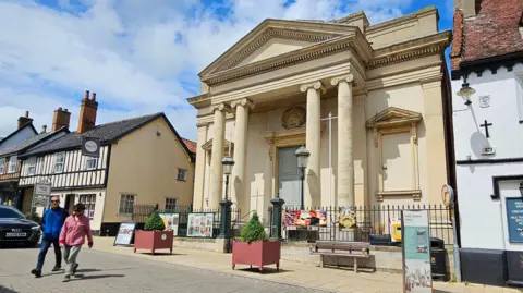 A sandstone-coloured building with elaborate columns flanking a large doorway.