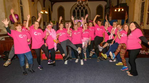 A group of women in pink t-shirts wave their arms in Arkengarthdale community hub