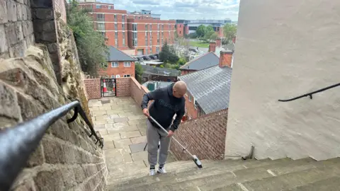 Volunteer Peter Smith cleaning the newly restored steps, which give a view over part of the city, with a broom.