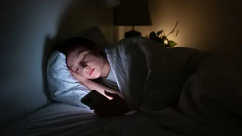 A woman lies in bed in a dark room looking at her phone