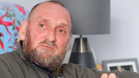 Phil Stevens - a white, bearded man staring towards the camera while sitting in his living room.