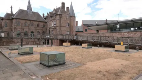Six glass cases near a visitor centre in a city centre. Behind then are old, brown buildings