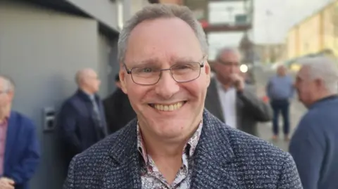 A man with glasses, a paisley shirt and a tweed coat.