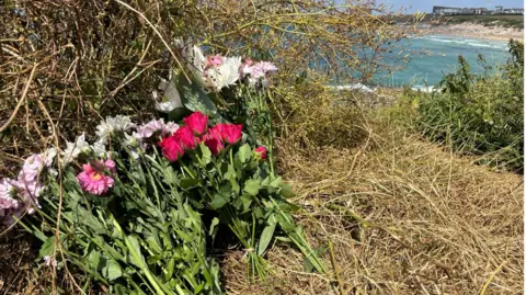 Pink and white flowers left on a cliff overlooking Fistral Beach in Cornwall.