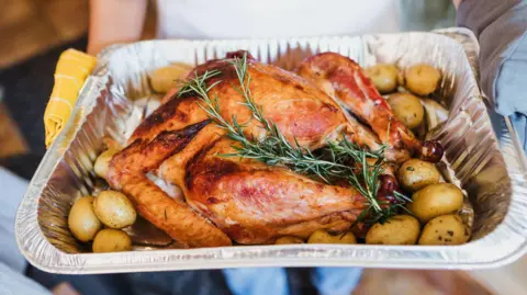 Getty Images A cooked turkey in a silver tray with potatoes and herbs around the side.