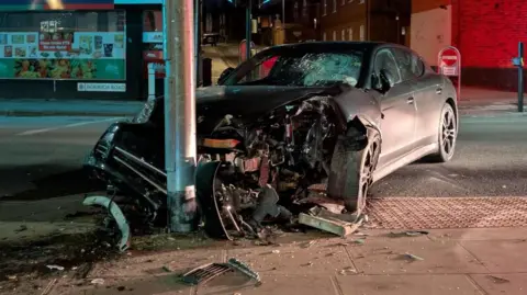 A Porsche vehicle suffered significant damage after crashing into a lamp-post in Ipswich town centre. The front and bonnet of the car is smashed, leaving one of the wheels exposed and debris across the pavement. The windscreen has also suffered damage. 