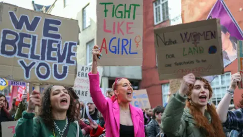 Getty Images Three protesters holding signs at a UK Women's March in Edinburgh in January, highlighting a rise in misogyny