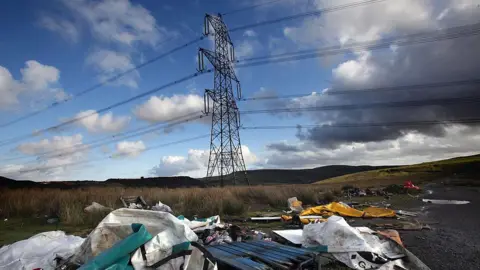 Getty Images Flytipping beneath electricity pylons in Merthyr Tydfil. Bags and furniture are visible.