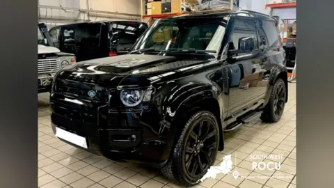 SWROCU A shiny black land rover in a warehouse with other vehicles.