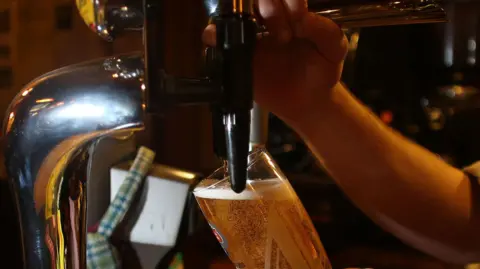 PA Media A close-up of a person pouring a pint on tap. 