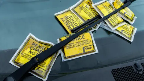 Multiple yellow parking tickets under a windscreen wiper.