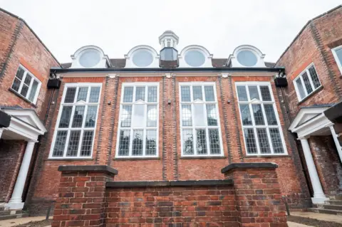 Amber Valley Borough Council Close up of the front of the school. Red brickwork framing four large rectangular windows with a cupola and four circular windows above. Doorways with decorative porticos sit on either side.