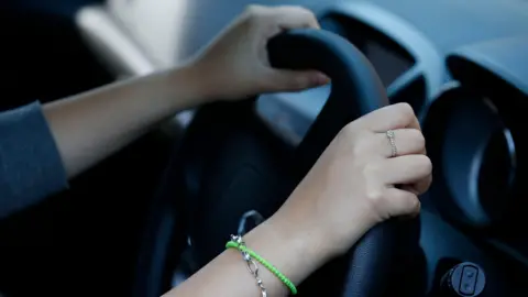PA Media Stock shot of a woman holding the steering wheel of her car. Just her hands and arms are pictured.