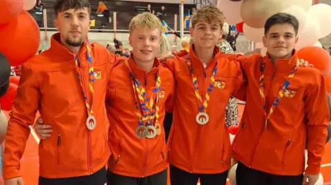 HELEN DUGGAN Four young men in Isle of Man team jackets with medal around their necks after winning in Orkney.