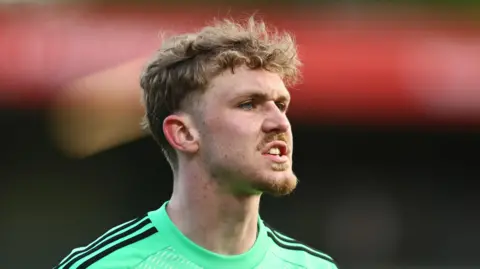 Matty Young playing for Salford City, wearing a lime green goalkeeper top and about to shout something.