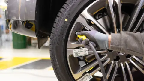 A person's hand is seen inflating a Land Rover tyre 
