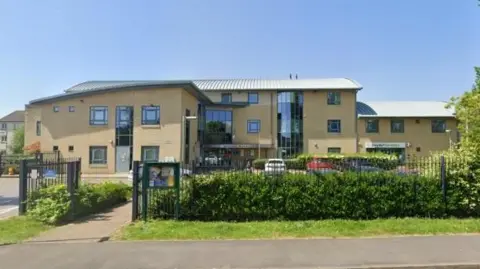 Google Hathaway Dental Practice on a sunny day. It is a large whitewashed brick building with lots of windows and a sloping roof.