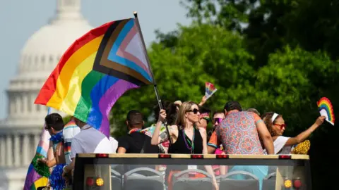 Parade participants wave rainbow flags from the top of a double decker tour bus as Capital Pride Parade makes its way down Pennsylvania Avenue in Washington DC. The dome of the US Capitol is in the background.