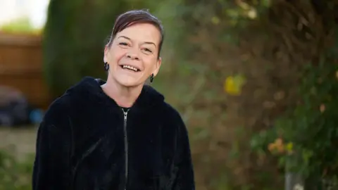 Shelter Amanda Wall. She was photographed outside wearing a black zip-up jacket. She has dark hair tied up and is wearing black hoop earrings. She is smiling at the camera. 