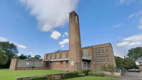 Google A 1950s-style brick church with a tall tower and a main building with boarded up windows