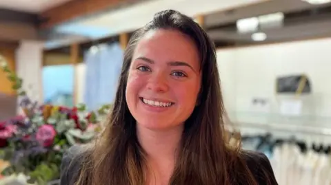 Retail assistant Jessica Kingsley, a white woman in her twenties with long brown hair. 