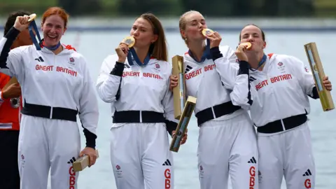 Reuters Four rowers wearing white tracksuits. All of them have a gold medal around their necks, holding it up or kissing it in victory