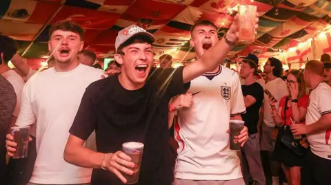 England supporters cheer after their team's first goal as they watch the television broadcast of the 2026 World Cup Group L football match between England and Panama, at The Clock pub in Hebburn, north-east England late on June 27, 2026.