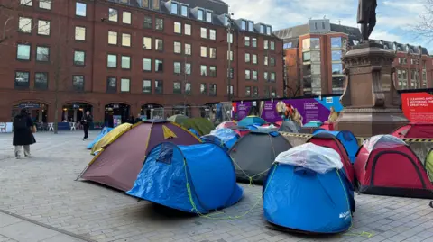 A collection of tents surround a large statue on a city Square. 