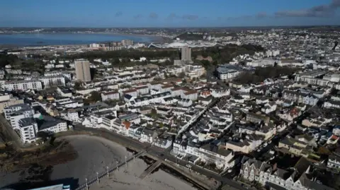 This is an aerial view of Jersey showing buildings, a beach and the sea on a mostly clear day.