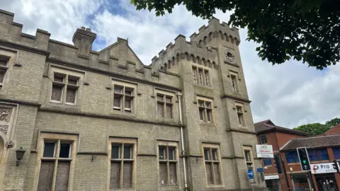 A view of the external part of Ipswich County Hall. Windows can be seen spanning three storeys while a clocktower can be seen at the end of the building.