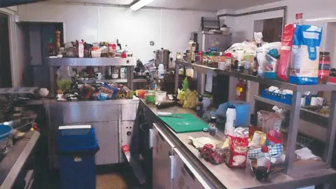 North Yorkshire Council A kitchen with mess everywhere, some items on the floor, food out in the open, messy chopping boards.