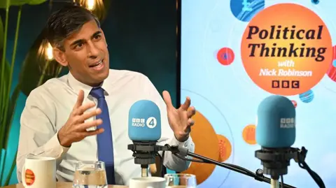 Rishi Sunak speaks into a BBC Radio 4 microphone in a BBC podcast studio during his interview on Political Thinking with Nick Robinson