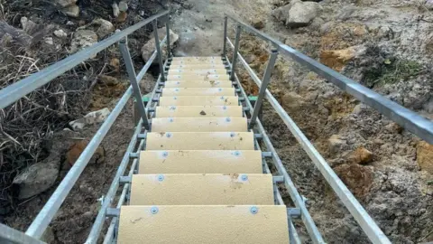 Metal flight of steps with cliff either side and pale yellow textured tread.