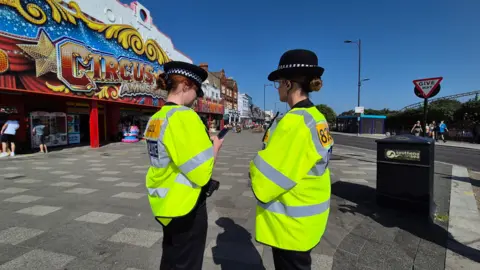 Stuart Woodward/BBC Two police officers in their uniforms at the seafront. It looks empty and there are shops in the background