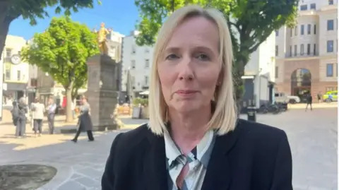 BBC Deputy Catherine Curtis is pictured in the royal square. She is wearing a black blazer and has blonde hair. 