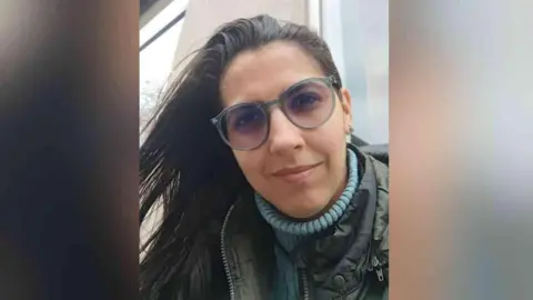 Family handout Vitória is looking at the camera up close. She is wearing a blue turtle neck jumper, a khaki or dark-coloured coat, has glasses on, and has brown hair.