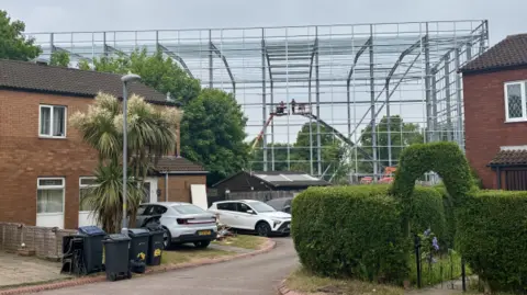 Metal structure behind houses in a street. The top of the frame rises above the height of the houses.