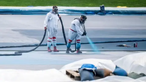 Reuters Workers in paint suits and gas masks spray-painting the pool surface blue