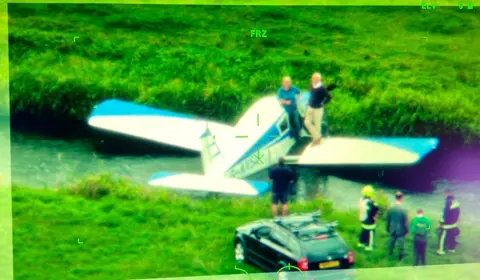 Small plane in a ditch in a field with emergency services nearby