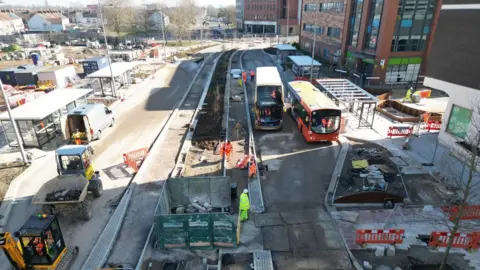 Swindon Borough Council Birds-eye view of a building site along a road to make it a bus interchange. Two buses test out a lane.