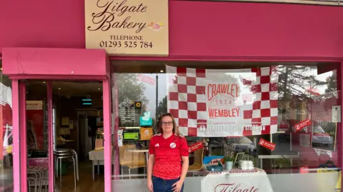 Hanna Neter/BBC Jane Kirkham with a Crawley flag in the window of her bakery