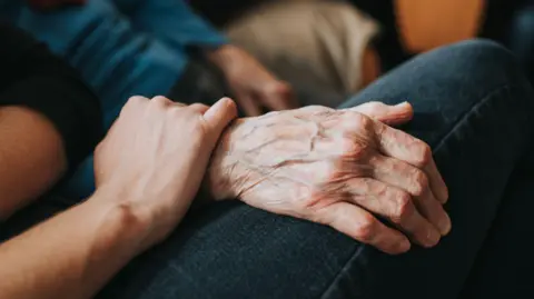 A younger person holding an older person's hand.