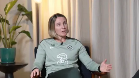 Sonia Bompastor wearing a pale green long sleeved top, sitting in chair.